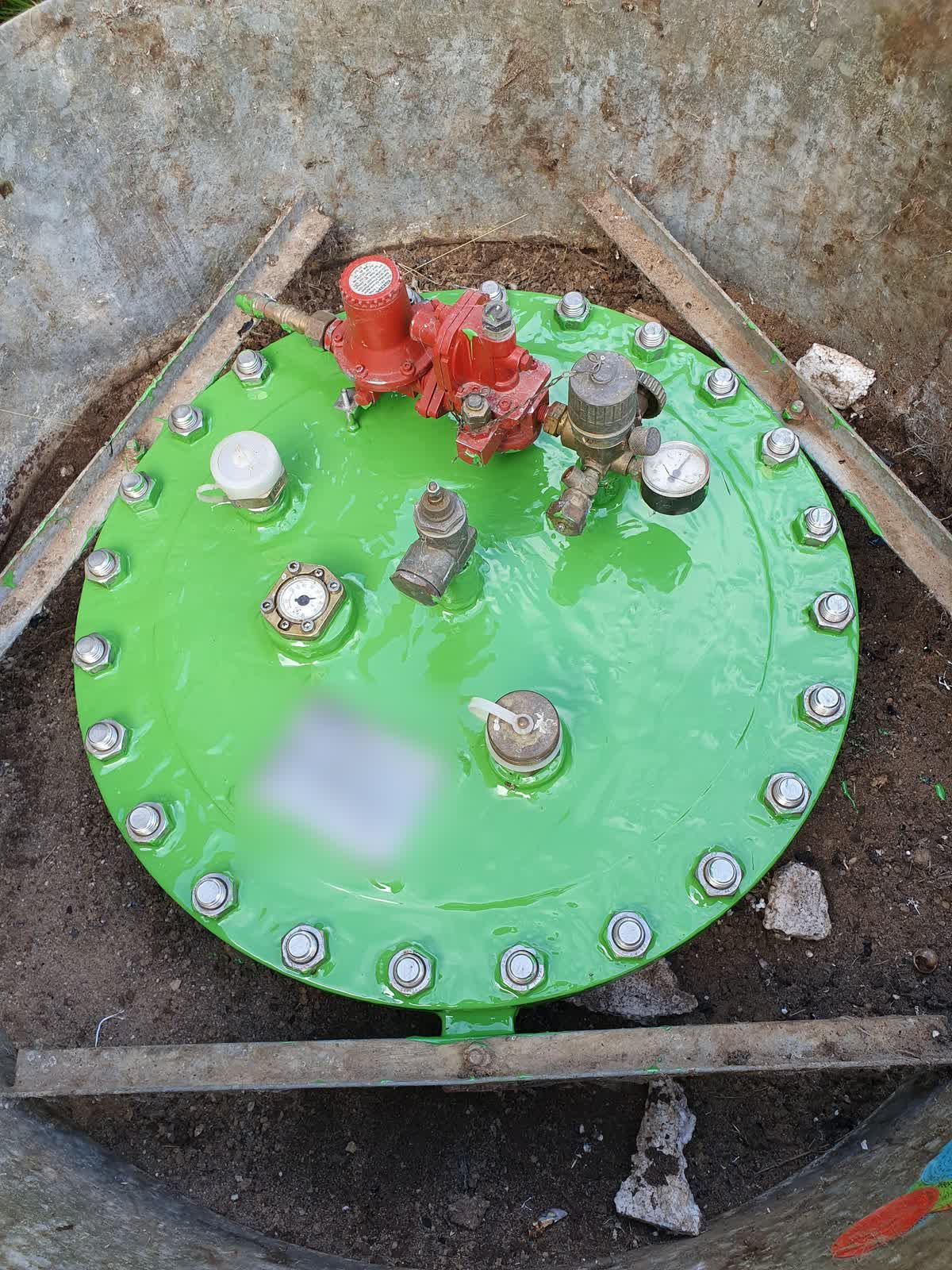 Blick in einen Haushaltsdomschacht: der Behälterkopf mit Armaturen, Manometer und Typenschild - beim erdgedeckten Behälter die einzige zugängliche Stelle